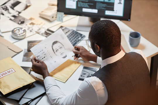 High angle view at Black male detective holding identikit photo of suspect while investigating case