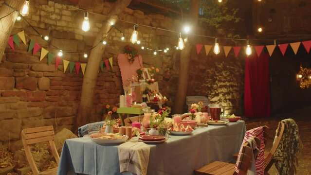 No people shot of beautifully set dining table decorated with orange marigold flowers and candles under outdoor string lights in cozy backyard on autumn eveningNo people shot of beautifully set dining