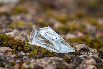 Macro of an isolated piece of glass from a broken bottle on the ground, shattered and sharp. Close-up that looks like a gemstone.