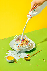 Milky breakfast. Woman pouring milk into cereal bowl, muesli with berries against green yellow background. Concept of healthy food, nutrition, pop art style, taste. Poster. Copy space for ad