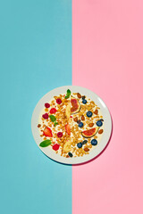 Delicious, healthy, sweet breakfast. Bowl with muesli and berries against blue pink background. Concept of healthy food, nutrition, pop art style, taste. Poster. Copy space for ad