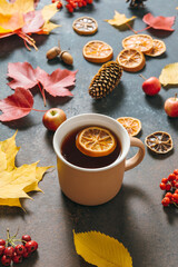 Autumn mood composition with cup of tea, fallen leaves, red berries, apples, cones on dark table background. Happy holidays, thanksgiving day, cozy home weekend. Hygge flat lay, top view, overhead.