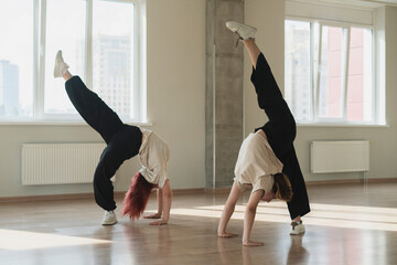 two girls doing synchrone acrobatic moves in the dance studio