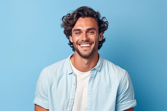 Portrait of a smiling young man with curly hair looking at camera isolated over blue background