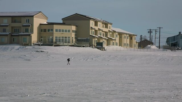 Man walking across frozen lake next to housing at Utqiagvik Barrow Alaska North Slope in the Arctic