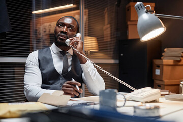 Portrait of African American man as male detective speaking by landline phone in office, copy space