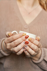Beautiful hands of a young woman with autumn manicure in brown and yellow colors on nails
