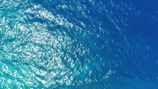 Drone top down static of shimmering light across blue ocean texture, half lit by sun