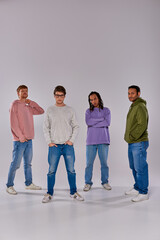 four young friends in casual trendy outfits standing looking at camera on grey backdrop, diversity
