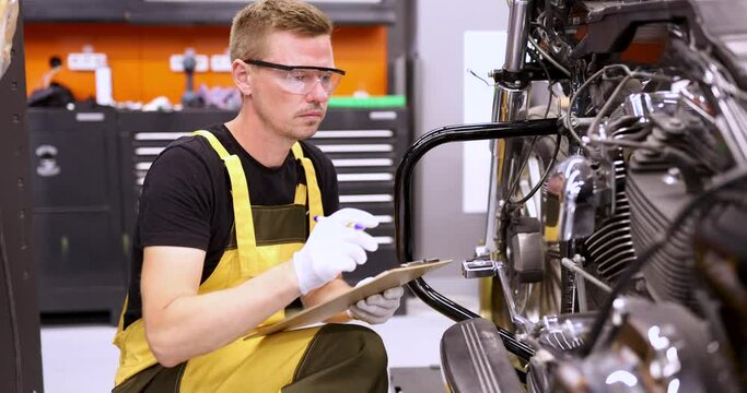 Male mechanic diagnoses parts on motorcycle at service center. Calculating motorcycle repair concept