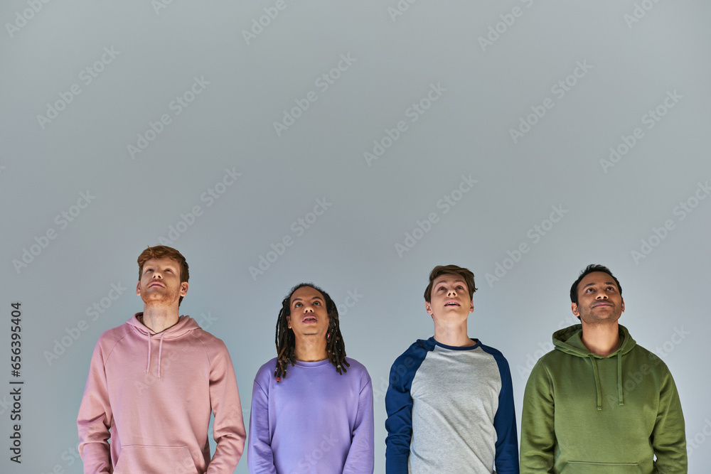 Wall mural four smiling young men in casual bright attire looking up on grey backdrop, cultural diversity