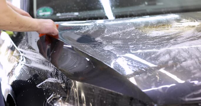 Man covering car with vinyl polyurethane tape closeup 4k movie. Car detailing services concept