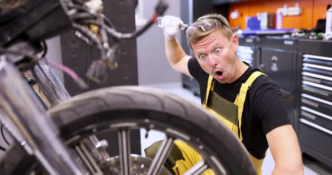 Surprised man repairman repairing motorcycle and scratching his head with wrench 4k movie. Motorcycle maintenance and repair problems concept