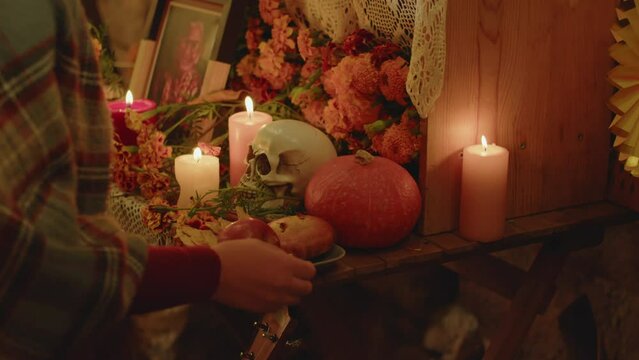 Cropped shot of unrecognizable woman putting plate with traditional treats on altar to demonstrate honor and respect to her departed family member on Day of the DeadCropped shot of unrecognizable woma