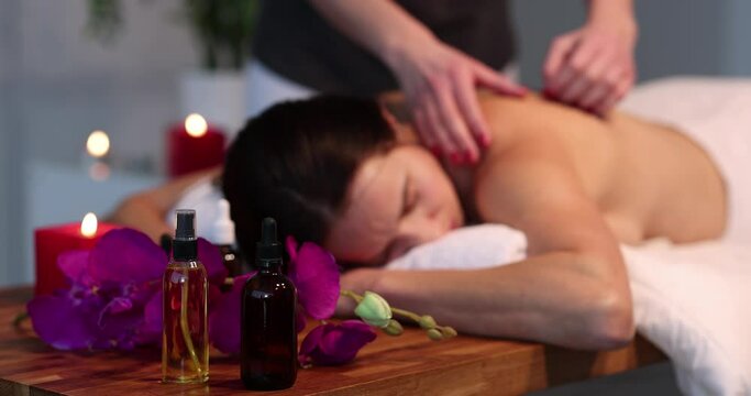 Jars of aromatic oils standing against background of masseur and woman in spa 4k movie. Professional cosmetics for massage concept