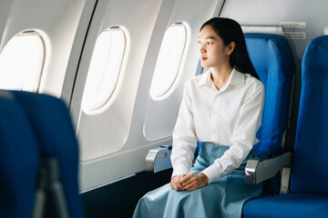 Asian woman sitting in a seat in airplane and looking out the window going on a trip vacation...