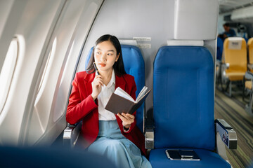 Young Asian executive excels in first class, multitasking with digital tablet, laptop and...