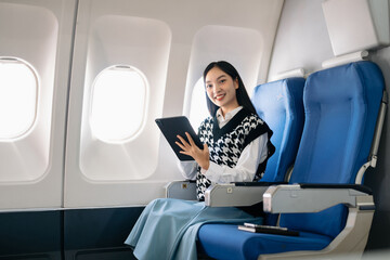 Attractive Asian female passenger of airplane sitting in comfortable seat while working laptop and tablet with mock up area using wireless connection. Travel in style, work with grace..