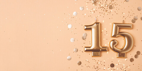 Gold candles in the form of number fifteen on peach background with confetti. 15 years celebration.