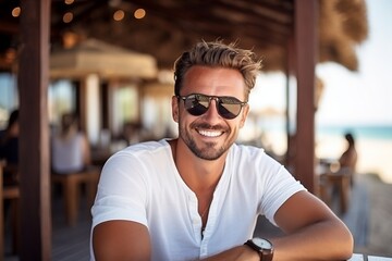 Portrait of a handsome young man wearing sunglasses and smiling at the beach - Powered by Adobe