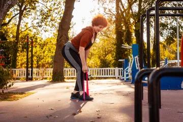 Fotobehang Adult Caucasian woman does stretching with elastic band on street. Healthy lifestyle and training in park. Autumn sunny weather © _KUBE_