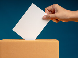 Election day. Hand voter holding ballot paper putting into the voting box at place election against...