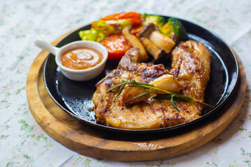 Delicious pork steak served with gravy and side dishes of red tomatoes, broccoli, mushrooms and...