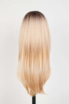 Natural looking blonde wig on white mannequin head. Long hair on the plastic wig holder isolated on white background, back view.