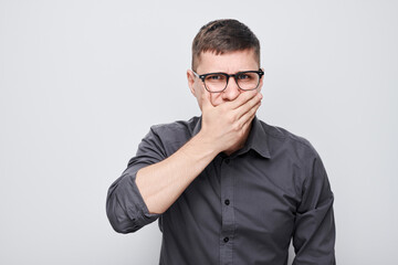Portrait of man covering his mouth with hand isolated on white studio background. Bad breath...