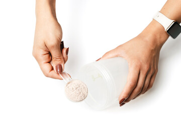 Woman's hands with measuring spoon puts portion of whey protein powder into a shaker, making...