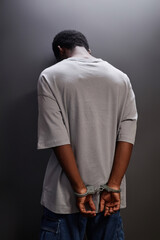 Back view of young Black man arrested standing by wall with handcuffs