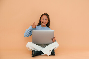 Sitting with laptop. Showing gesture. Cute young girl is in the studio against background