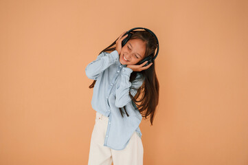 In headphones, positive energy. Cute young girl is in the studio against background