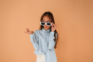 Funny facial expression and emotions. In sunglasses. Cute young girl is in the studio against...
