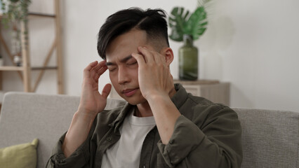 shoulder shot anxious asian man experiencing headache is rubbing temples while worrying about future during self isolation in the living room at home