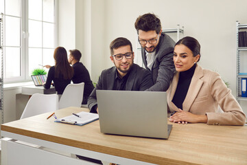 Two interns in office learning new computer software while listening to male business trainer. Male...