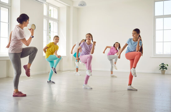 Group of kids at dance class. Children do sports exercises with professional instructor. Little girl dancers do movements together with coach choreographer in white dance hall, gym or fitness center