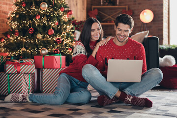Full body photo of sit cute young couple relaxing while man browsing internet to order christmas gifts for kids online on xmas background