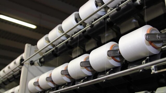 Spools With Threads Spinning at Textile Factory. Yarn is produced by spinning raw fibers of cotton or other materials to produce long strands suitable for use in the production of textiles.