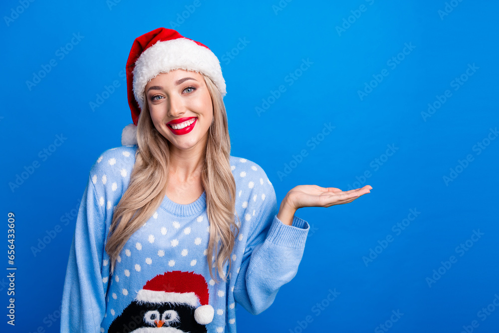 Poster photo portrait of lovely blonde young lady palm hold empty space wear penguin sweater x-mas hat isol