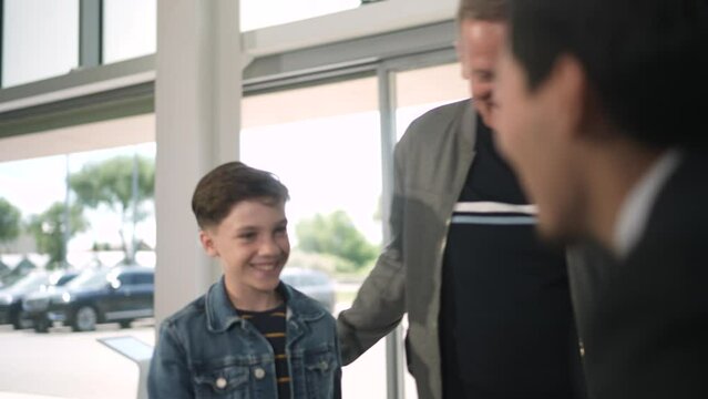 Young father and son arriving at the car dealership and exploring their options with a car salesmen