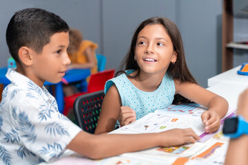 Teacher and school student children studying at desk in educational classroom, writing in notebook, reading book. Group of diverse classmates learning. Academic Concept.