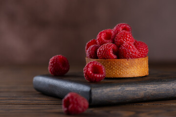 Tartlet with raspberries and cream, fresh dessert for breakfast on a brown background.
