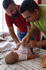 Vertical image of a couple two gay men changing their adopted son's clothes on the bed in their room
