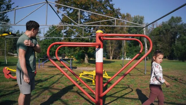 Father with child girl doing sports outdoors in a park gym. Parallel bars exercises. Modern parenthood with active lifestyle