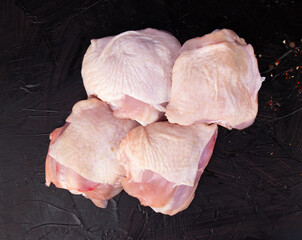 Fresh raw chicken thighs for cooking on a black background in a close-up shot.
