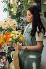 young woman florist wearing apron making bouquet at flower shop
