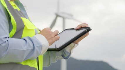 Engineer with electronic tablet near windmill: technical consideration for future green energy. Technical analysis and study indicators. Statistics and accounting data, results performance indicators - Powered by Adobe