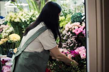 young woman florist wearing apron making bouquet at flower shop