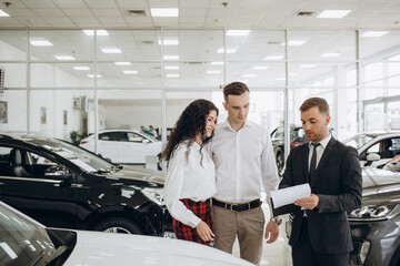 Couple and the dealer selling cars look the car in the showroom.